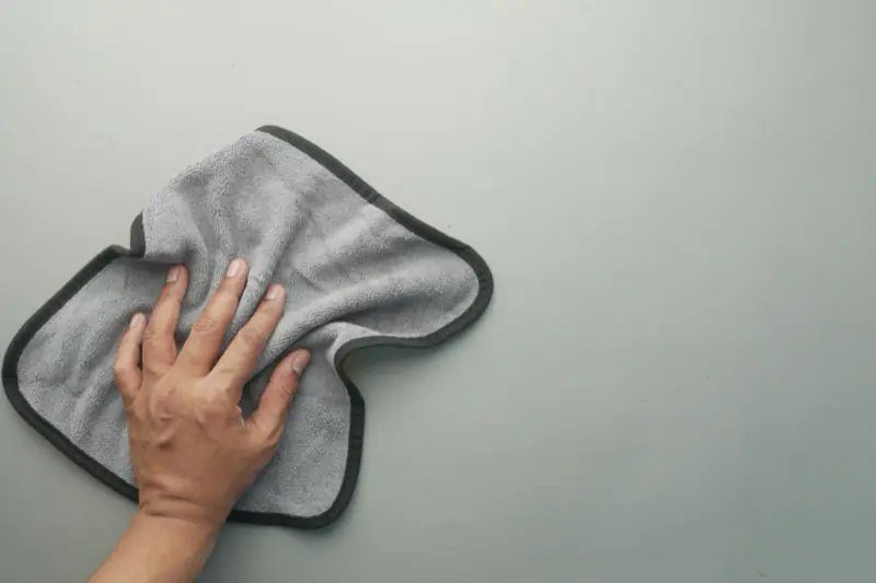 Hand wischt mit einem grauen Mikrofasertuch über eine helle Fläche