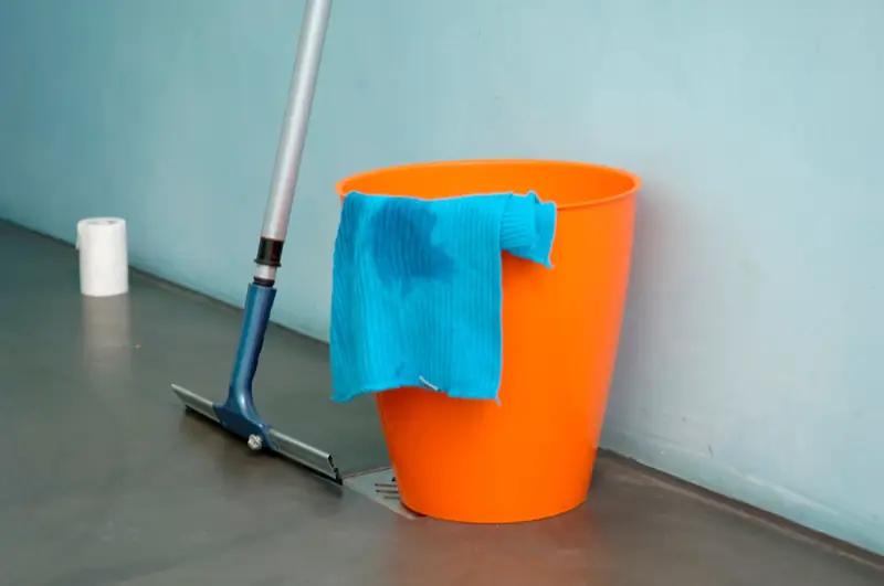 Orangefarbener Eimer mit blauem Tuch und Wischer an einer Wand